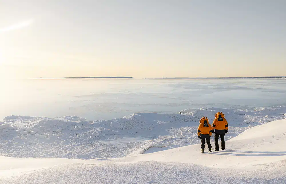 Voyageurs sur rives enneigées regardant vers la mer gelée